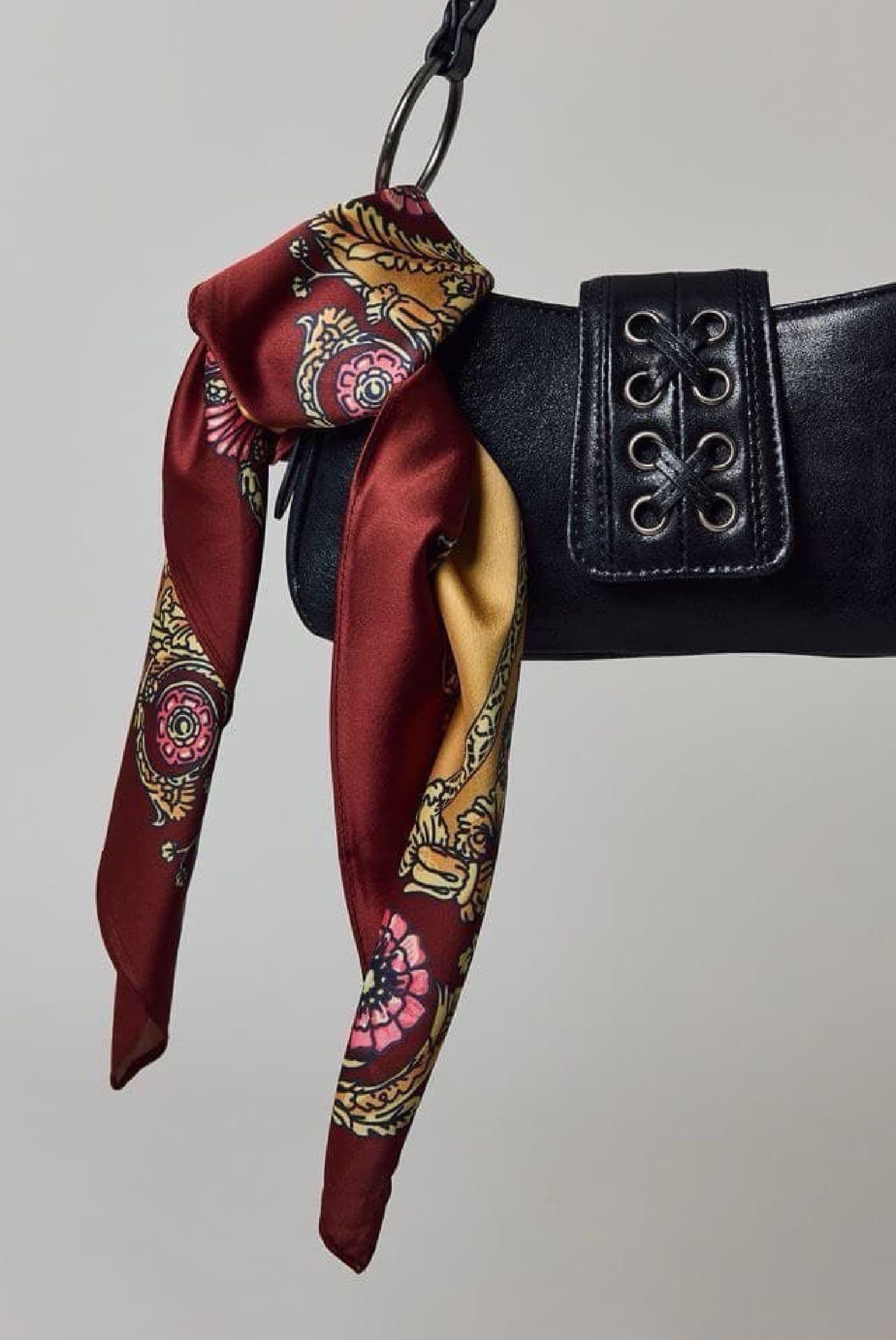 A close-up of the Wine Paisley silk scarf knotted around a leather bag